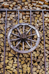 Fototapeta na wymiar vintage wooden wheel on the background of a wooden woodpile of firewood