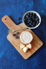 Close up photo of French mild cheese and juicy organic berries on a table. Top view photo of tasty appetizer. Food still life photo. Textured background with copy space. 