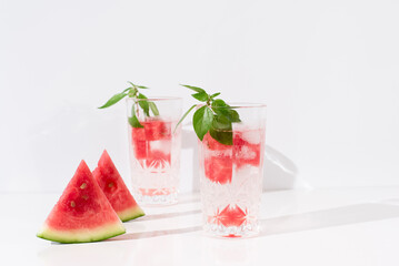Dos vasos de zumo de sandía con trozos de sandia y hielo sobre fondo claro
