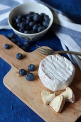 Still life with Brie cheese, blueberry and wooden board. Blue textured background with copy space. 