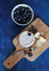 Still life with blueberry and cheese on wooden board. Fresh food on a table. French cuisine. 