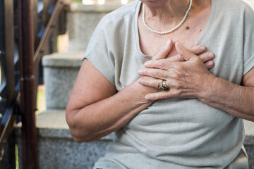 Elderly woman sitting on stairs and holding hands on chest due short breath. Upset stressed senior woman feeling pain ache touching chest having heart attack