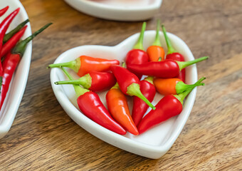 set of chili peppers mini pods in a plate heart close-up on a wooden background