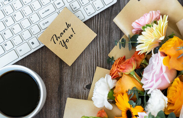 Thank you note on top of computer keyboard with cup of coffee and mixed flower bouquet