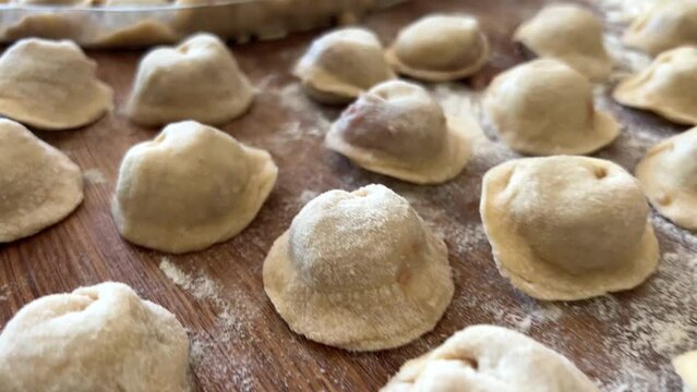 grandmother prepares delicious dumplings or pies or dumplings for her grandson she shakes dough, cuts it into pieces and sculpts on the table there are circles of dough she is sprinkled with flour