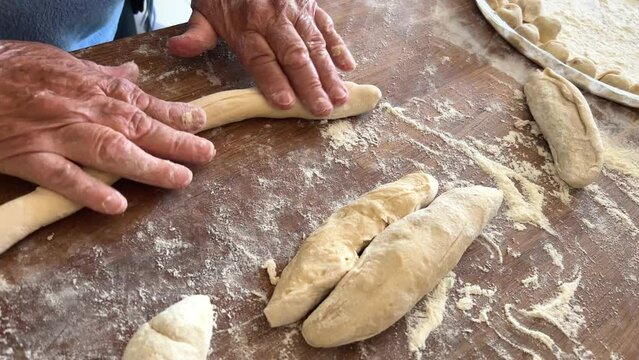kind old hands of an elderly woman grandmother roll out the dough she will cook pies and bake something or boil dumplings or dumplings on a wooden surface soft fresh dough. High quality 4k footage