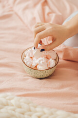 A woman's hand takes a meringue from a plate on a peach-colored sheet