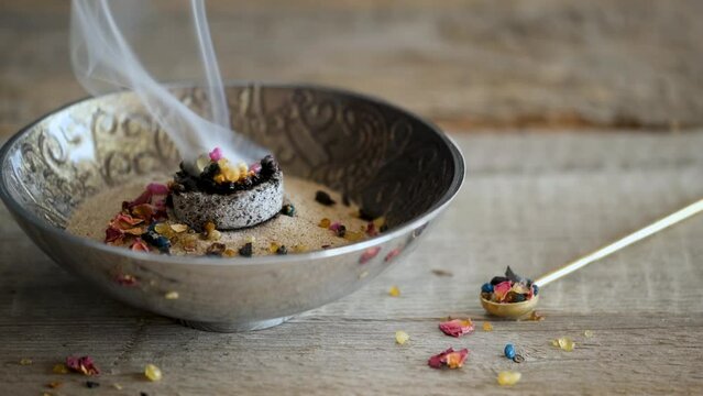 Mixture of aromatic incense resin, frankincense (olibanum), styrax and rose blossom petals burning on hot charcoal in a bowl on wooden surface
