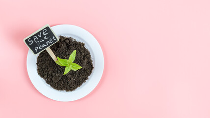 A plastic white plate with black earth, a green sprout and a peg with the inscription: save our planet .