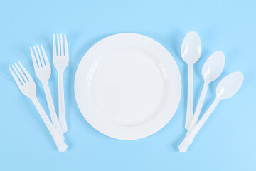 Empty plastic plate with forks and spoons on the sides on a blue.