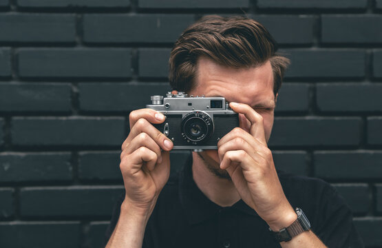 A young man takes a photo with a vintage film camera.