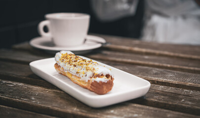 Cup of coffee and eclair on a wooden table close-up.