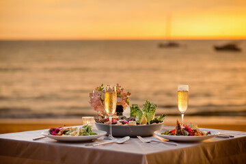 Romantic sunset dinner on beach. Table honeymoon set for two with luxurious food, glasses of...