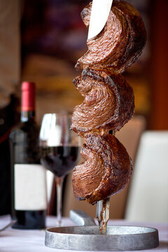 Brazilian Picanha on a skewer with wine in the background in a restaurant setting