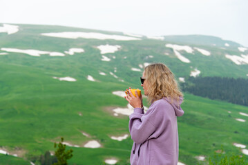 A young woman with a yellow mug in her hands looks at a plateau in the mountains. Vacation in the mountains. Nature. Early morning. Beauty.