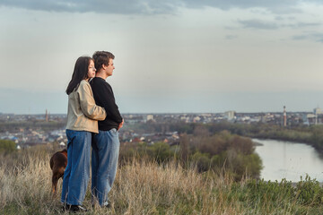 a couple in love hugs while relaxing outside the city on a walk in the rays of sunset, their big dog is with them