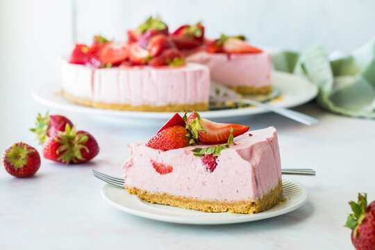 A slice of strawberry cheesecake with the rest of the cake in behind.