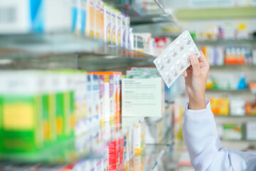 Female pharmacist wearing lab coat in a modern pharmacy drugstore., selecting a medicine for customer..