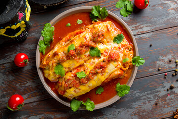 Enchilada with beef with tomato sauce on wooden table, mexican kitchen top view