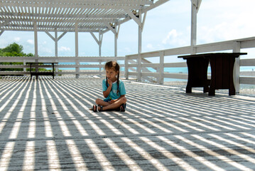 A little girl in the shade of a gazebo plays with stones. She plays of light and shadow. Childhood.