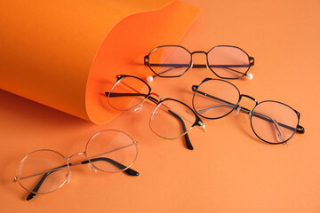 rolles orange paper and several pairs of stylish glasses, eyeglass frames in fashion trend, bright...