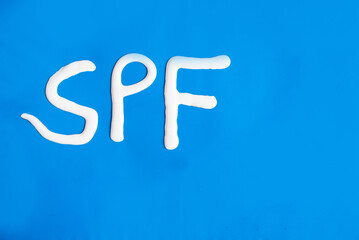 Las letras SPF escritas con protector solar sobre un fondo azul - obrazy, fototapety, plakaty