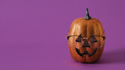 trendy stylish glasses on the face of a decorative shiny orange pumpkin on a purple background