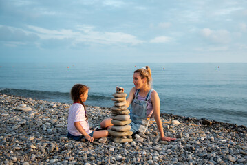A mother and daughter 6 years old on the beach build a castle of stones. They socialize and have...