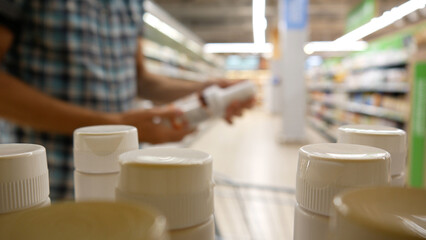 Close-up of many plastic bottles with confectionery sauce or milk coctail and a man with a shopping trolley takes one