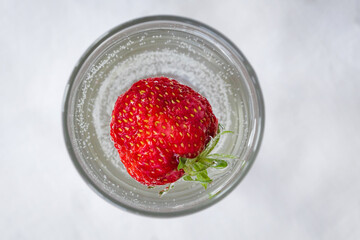 Strawberry cocktail from top view, isolated on white background. A large whole strawberry in a glass of sparkling mineral soda water. Cold summer drink