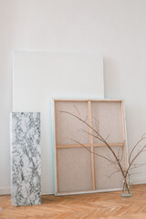 Aesthetic interior shot. Canvases, branches in vase in art studio. Minimal style, light colors.