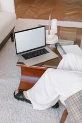 Laptop computer blank white screen in interior. Close up of businesswoman in stylish outfit working in cozy living room.