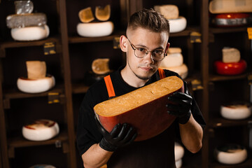 Portrait of handsome cheese sommelier with cheese gouda. Fashion worker in cheese shop. Snack tasty piece of cheese for appetizer.