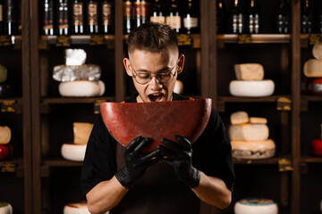 Handsome cheese sommelier holding and jokes with limited gouda cheese. Snack tasty piece of cheese for appetizer. Hungry man.