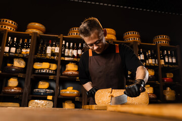 Handsome cheese sommelier cut limited gouda with knife. Bearded hipster in fashion glasses working...