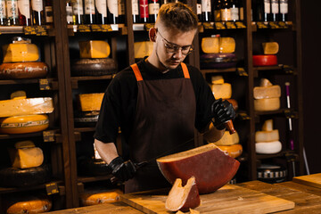 Handsome cheese sommelier with big knife for cut cheese. Bearded hipster in fashion glasses working in cheese shop. Creative idea for advertising.