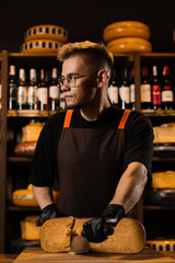 Handsome man worker of cheese shop cut limited gouda with knife. Cheese sommelier working in cheese...