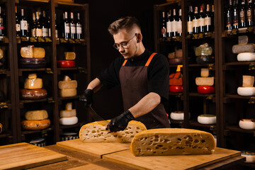 Limited maasdam cheese wheel cutting cheese in store. Cheese sommelier cuts yellow cheese wheel cut in half with a knife on the table.