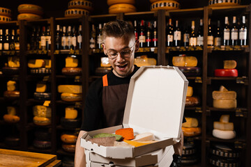 Cheese Sommelier holding many boxex with mix of young Gouda, young goat, lavander cheese and green and red pesto cheeses on the table. Creative idea for advertising a cheese shop.