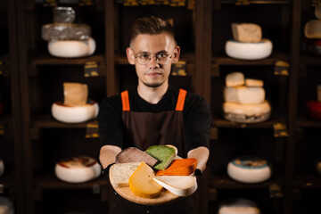 Cheese Sommelier holding plate with mix of young Gouda, young goat, lavander cheese and green and red pesto cheeses on the table. Creative idea for advertising a cheese shop.