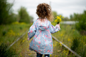 A little girl walks along the grassy railroad tracks. Ecology. The concept of the victory of nature over the vitality of man. Nature takes its toll.