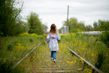 A little girl walks along the grassy railroad tracks. Ecology. The concept of the victory of nature over the vitality of man. Nature takes its toll.