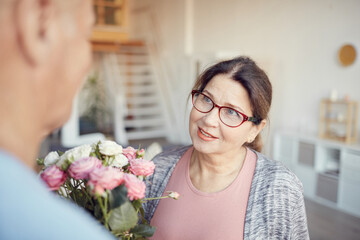 Smiling charming senior lady in eyeglasses receiving tender bouquet from husband on Valentines day