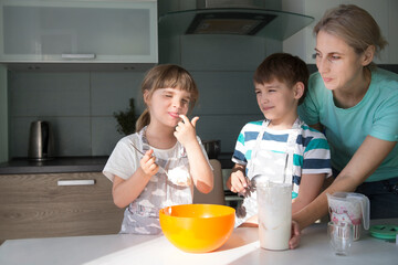 mom and two kids are cooking pie and having fun in the kitchen. casual lifestyle in real life interior. playful siblings helping to mother.  Concept of friendly family. Family spends time together