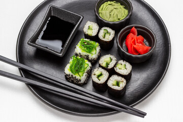 Sushi set, wasabi, soy sauce and black chopsticks on black round plate.