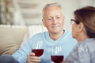 Content handsome elderly man with wineglass listening to wife while enjoying romantic time with loved person