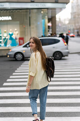 Girl crosses the road at the pedestrian crossing looking over her shoulder. Teenager against the backdrop of busy street.