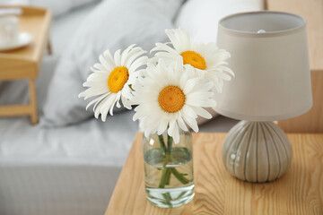 Fototapeta na wymiar Bouquet of beautiful daisy flowers and lamp on nightstand in bedroom
