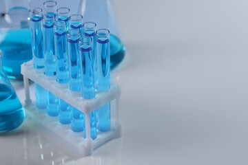 Laboratory glassware with blue liquid on light background. Space for text