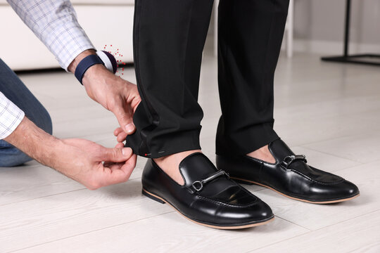 Professional tailor measuring length of client's trousers in atelier, closeup